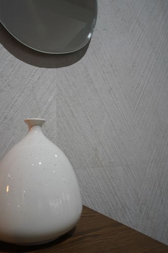 A vertical closeup shot of a white ceramic pot on a wooden surface in front of the wall