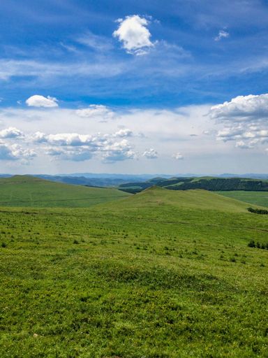 A vertical of lush green hills under a cloudy blue sky on a sunny day