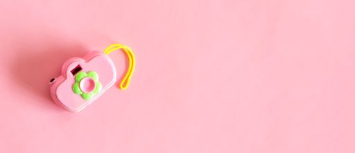 An isolated toy camera, pink color, on pink background. Top view.