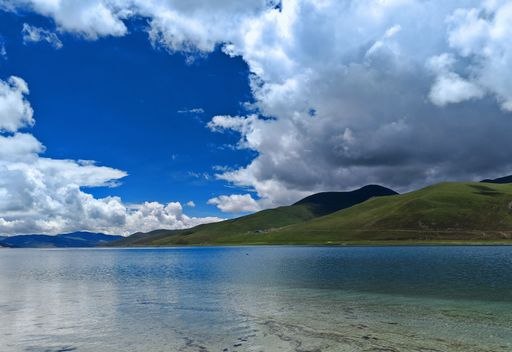 A scenic landscape featuring the Yamdrok Lake under a bright sky in Tibet