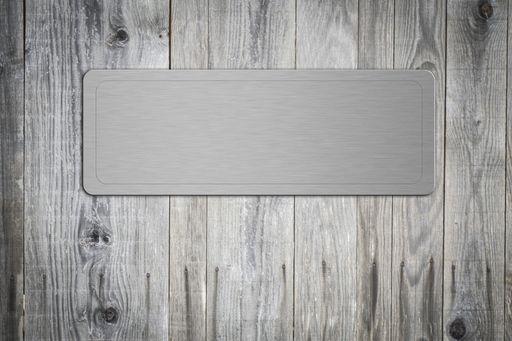 A closeup of a blank brushed iron nameplate on an old wooden door
