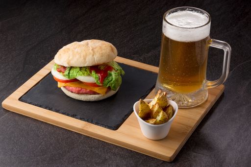 A delicious burger with potatoes and a glass of beer served on a wooden board