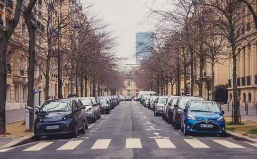 A shot of colorful cars standing on the sides of a road with a crosswalk in Paris, France
