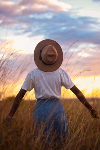 A person wearing a hat standing in a field looking up at the sunset sky.