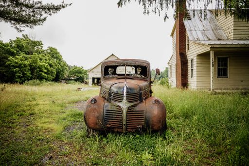 The two skeletons sitting in the driver's seat of a vintage parked car