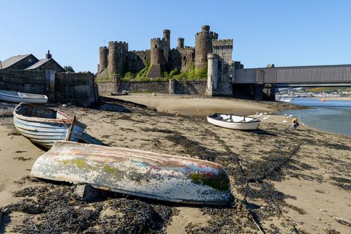 A closeup shot of Conway castle near the beach with old boats in the blue sky background, North Wales UK