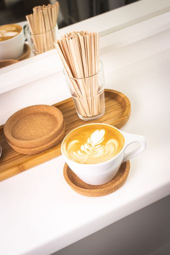 A closeup of a white mug of latte coffee on a wooden surface under the bright light