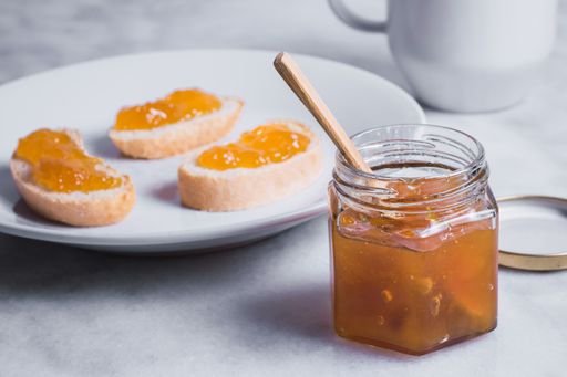 An open jar of honey with a honey dipper in it next to a ceramic plate containing honeyed toast bread