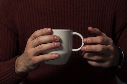 A man in a red sweater holding a hot cup of tea in his hand