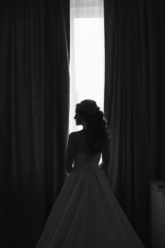 A full-length shot of a bride standing in profile, admiring the view from a tall window in her wedding dress
