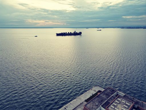 An aged seafaring vessel navigates the open sea as the sun sets, silhouetting the sails against a sky of colorful hues