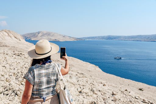 Young tourist wearing summer clothes and sun hat standing on ridge overlooking amazing coastline and sea on Pag island in Croatia.