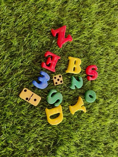 A top view of the colorful plastic alphabets, dice, and a domino on green grass in a lawn