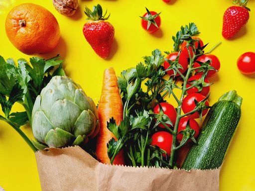 The closeup of fruits and vegetables in grocery paper bag against yellow background