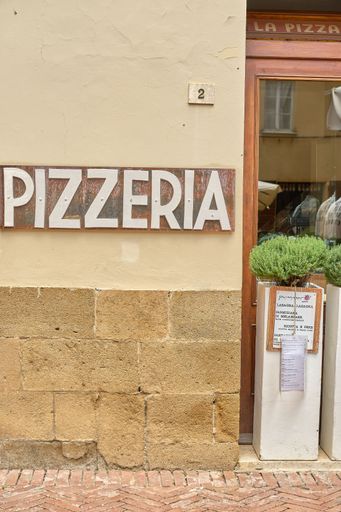An exterior shot of a brick pizza shop with the word "Pizzeria" painted in white on the side of the building