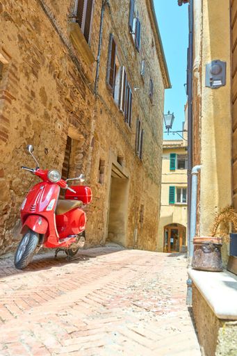 A bright red Vespa scooter is parked alongside a row of buildings with white framed windows