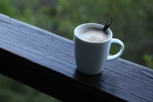 A selective focus shot of foamy coffee in a mug on a wooden balcony fence