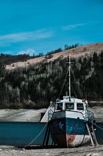 A vertical shot of a ship on the beach surrounded by hills and sea under the sunlight and a blue sky