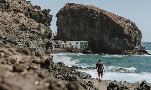 A selective focus shot of a male standing on a rocky beach surrounded with high cliffs in Spain