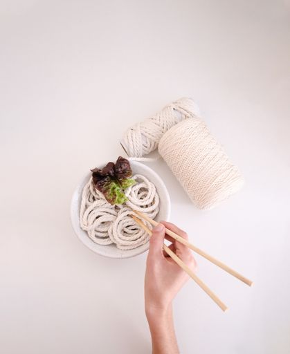 A creative shot of yarn noodles in a bowl with a lettuce leaf and a woman's hand holding chopsticks