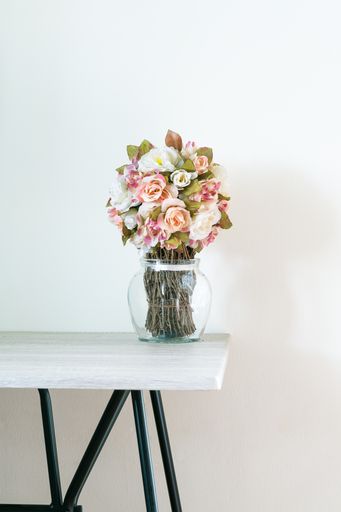 A vertical shot of artificial flowers bouquet in a transparent vase on a wooden table