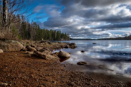 A high angle shot of big stones on the shore of the lake with the reflection of clouds in the water