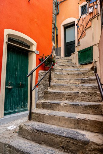 A staircase leading to a vibrant green entrance door set against a warm orange wall of a building.