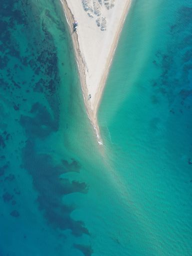 An aerial shot captures a stunning beach scene featuring a beach umbrella and a boat floating in the turquoise waters of the ocean