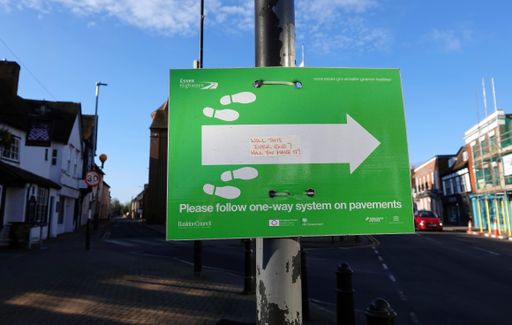 A green sign from the council with an arrow and footprints instructing the public to follow a one way system on pavements.