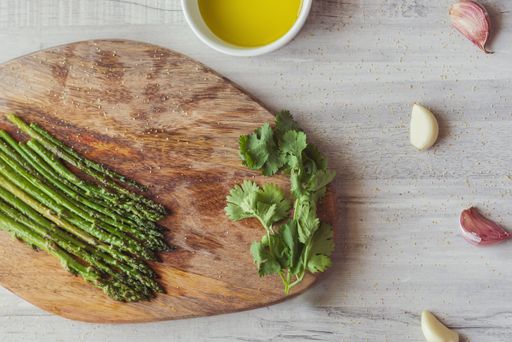 A top view of green asparaguses with a bowl of yolk and other ingredients on a wooden board