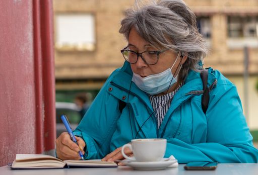 white haired woman drinking coffee at the bar while writing and looking at the phone
