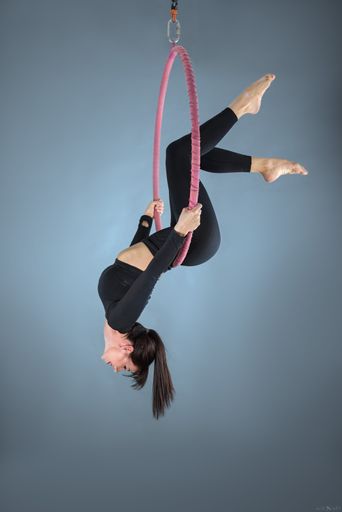 A young woman hangs upside down from a pink ring in a black shirt performing Aerial yoga