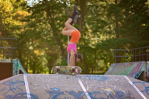 A young female doing a handstand at the skate park on a ramp next to a Tempish skateboard