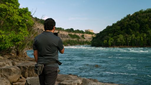 A man standing near a river, capturing photographs with a digital camera