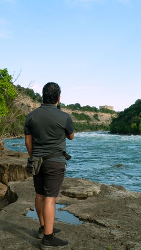 A man standing near a river, capturing photographs with a digital camera