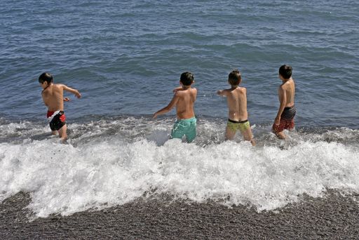 four children playing with the waves at the shore of a lake