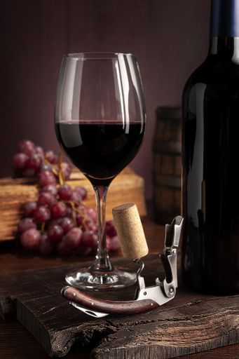 The glass of red wine and corkscrew with grapes on the background
