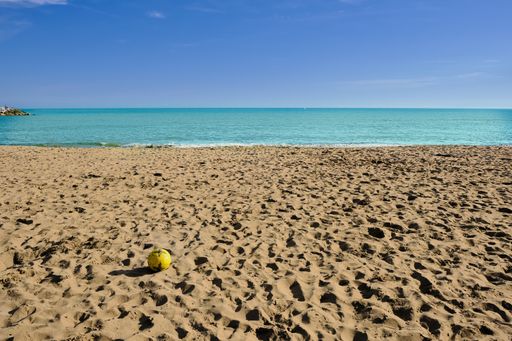 A small yellow ball on the sandy beach with the sea in the background and sky in Cabopino, Marbella, Malaga