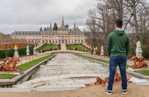 Young man in jeans and sweatshirt of Caucasian origin has spectacular views of the Royal Palace of San Idelfonso on a cloudy autumn day. Segovia.