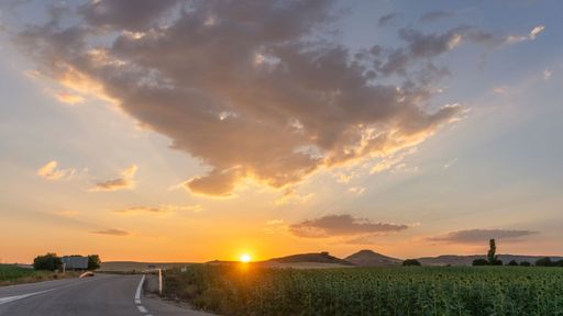 Rural road and sunset with the sun setting over the mountains.