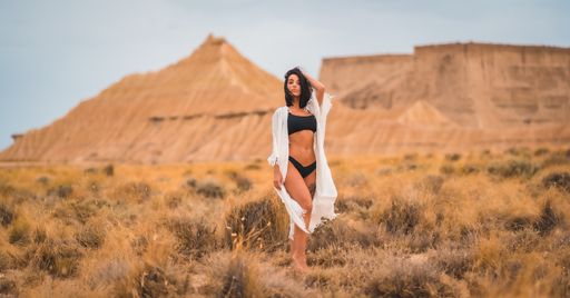 A brunette Caucasian model girl in a white dress and black bikini in the Bardenas Reales desert one summer afternoon