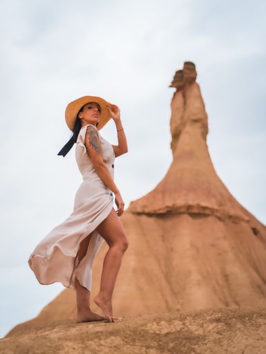 A brunette Caucasian model with a white dress and a straw hat in the Castildetierra of the Bardenas Reales desert, Navarra. Spain