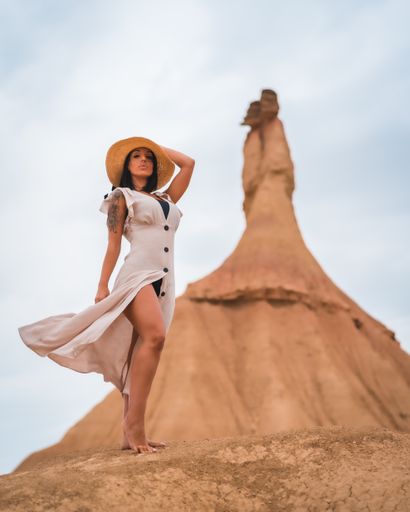 A brunette Caucasian model in a white dress and straw hat in the Bardenas Reales desert, Navarra. Spain