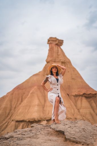A brunette Caucasian girl in an explorer outfit with a white dress and a straw hat in a beautiful desert on a cloudy afternoon