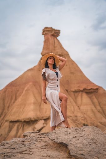 A brunette Caucasian girl in an explorer outfit with a white dress and a straw hat in a beautiful desert on a cloudy afternoon