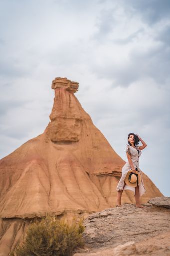 A brunette Caucasian girl in an explorer outfit with a white dress and a straw hat in a beautiful desert on a cloudy afternoon