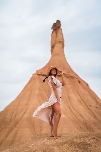 A brunette Caucasian model in a white dress and straw hat in the Bardenas Reales desert, Navarra. Spain