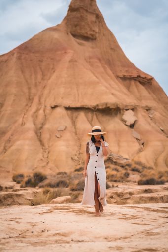 A brunette Caucasian girl with an explorer outfit with a white dress walking enjoying the desert of Las Bardenas Reales in Navarra. Spain