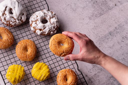 A man's hand holding a delicious donut in the bakery full of glazed donuts of San Isidro