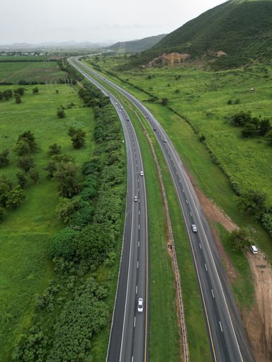 An aerial view of a tree-lined highway leading to a vast expanse of green grass in the distance